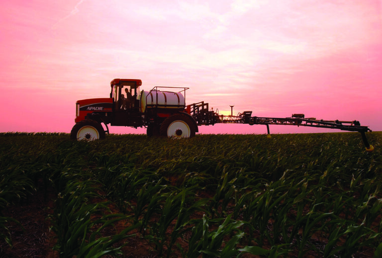 used apache sprayer being used in field with pink sunset in sky